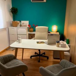 Imagen de despacho con mesa y silla de color blanco, dos butacas en frente de color gris y pared del fondo azul cobalto corporativo